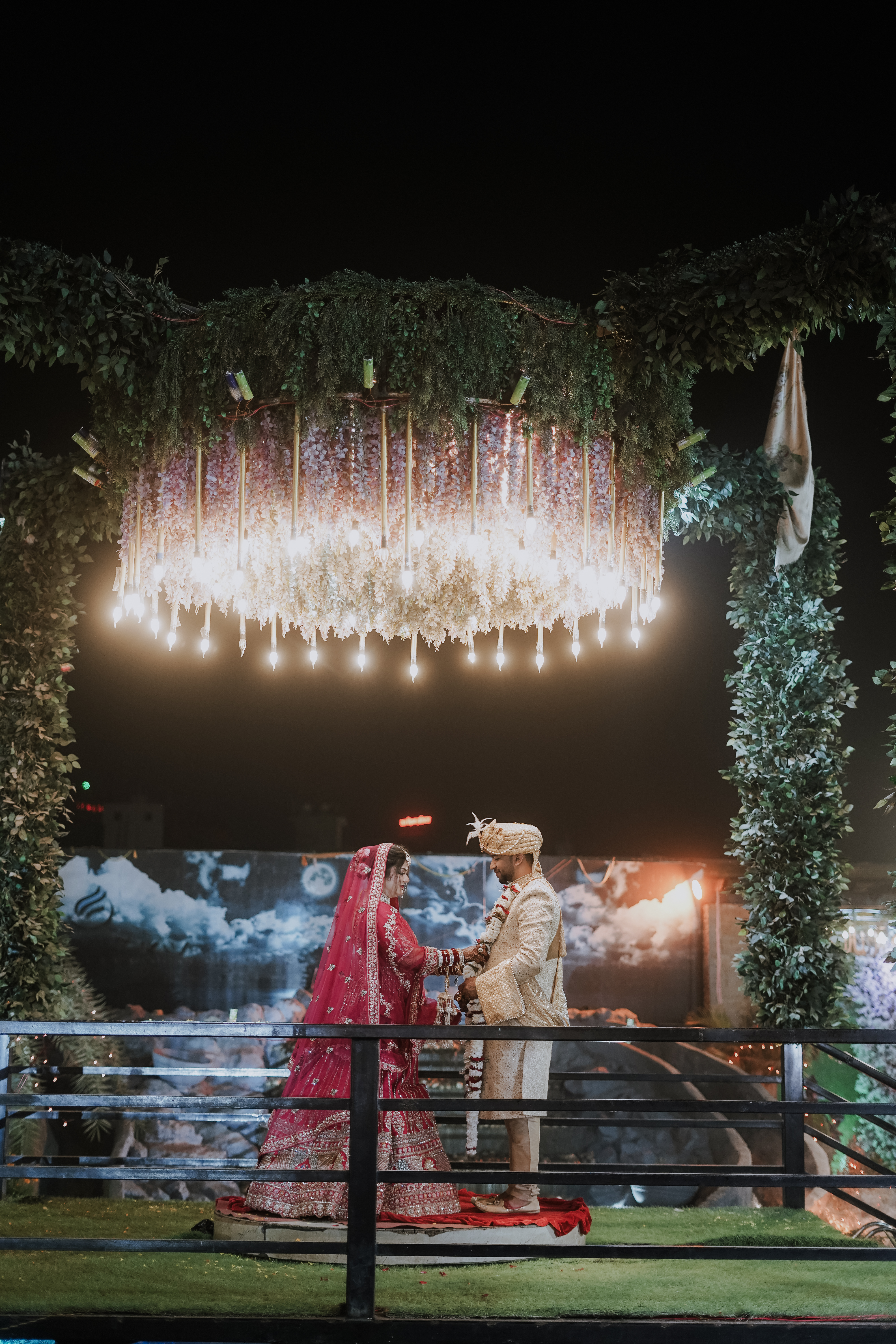 Authentic Varmala garland ceremony beneath illuminated floral chandelier and greenery arch