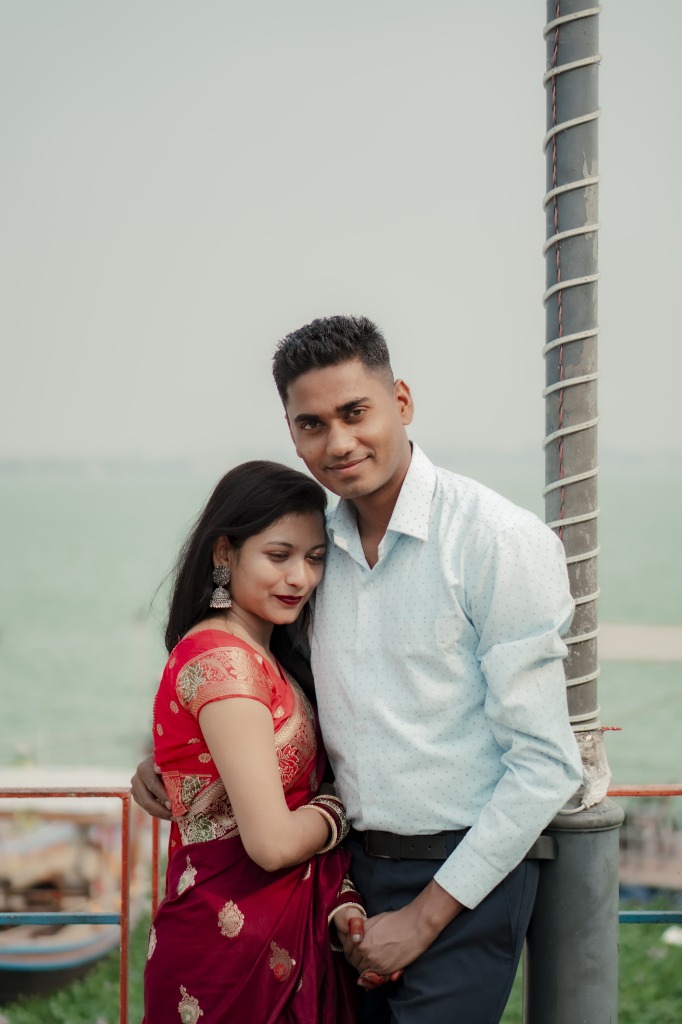 Bride Yasmin in crimson banarasi silk leaning on Groom Faiz by tranquil lake promenade